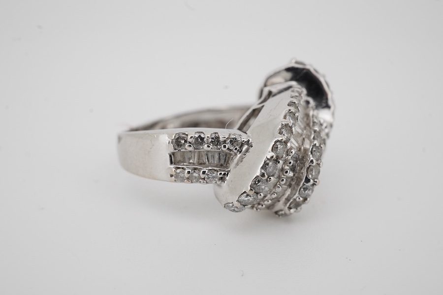 A modern white metal stamped 14k, tapered baguette and round cut diamond cluster set scrolling crossover dress ring, size K, gross weight 5,5 grams. Condition - fair to good